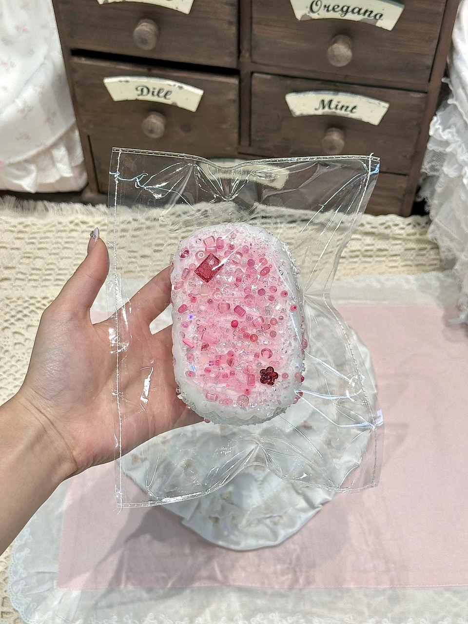 Pink and white latte art senbei squishy held in a hand, showing the patterned surface and real scale